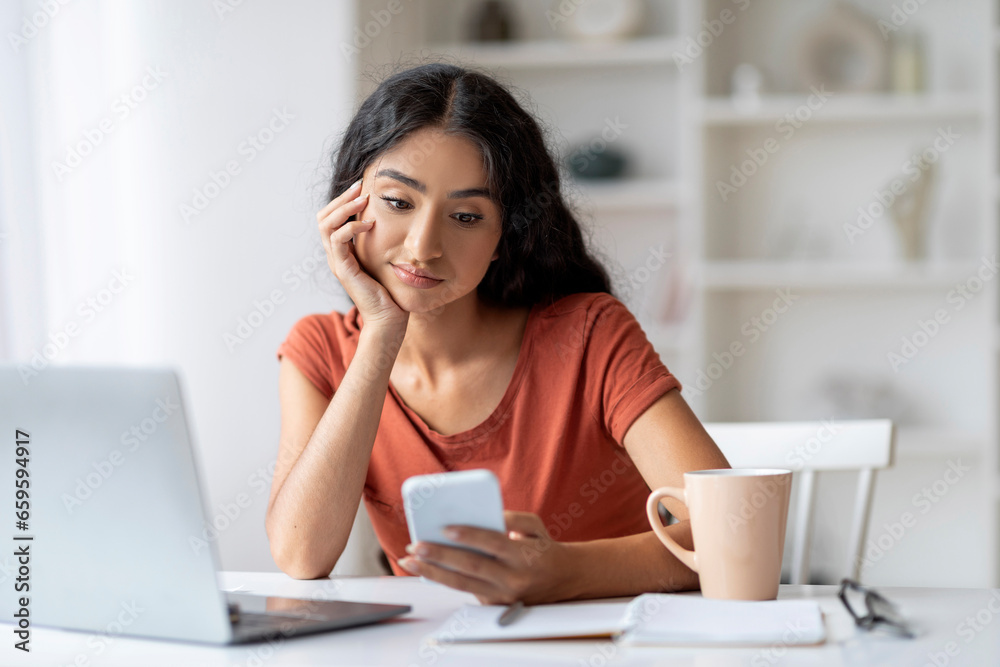 Attractive young eastern lady independent contractor using phone at home Attractive young eastern lady independent contractor using phone at home