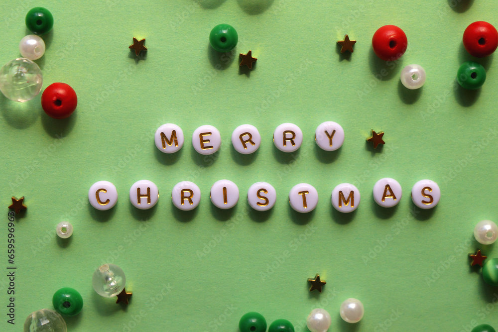 Various beads with Merry Christmas caption on green background. Top view. Various beads with Merry Christmas caption on green background. Top view.