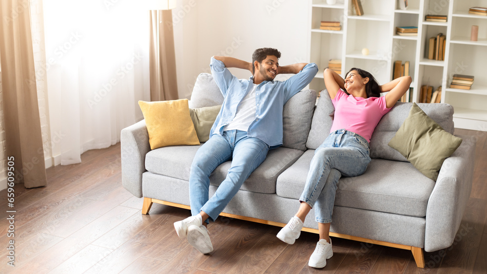 Relaxed indian couple smiling at each other while resting on couch at home
