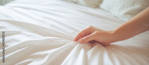 Woman arranging sheet on bed in bedroom or maid making bed in hotel room