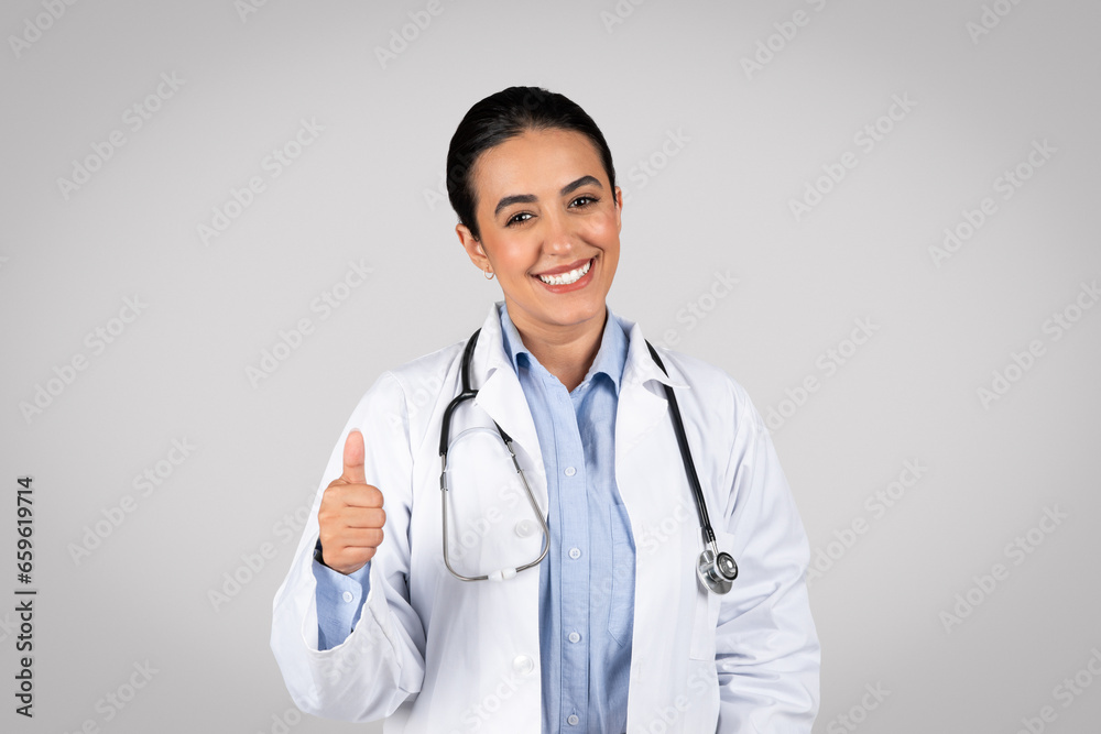 Smiling woman doctor giving thumb up in studio, approving medical offer Smiling woman doctor giving thumb up in studio, approving medical offer