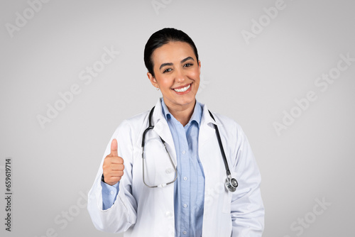 Smiling woman doctor giving thumb up in studio  approving medical offer