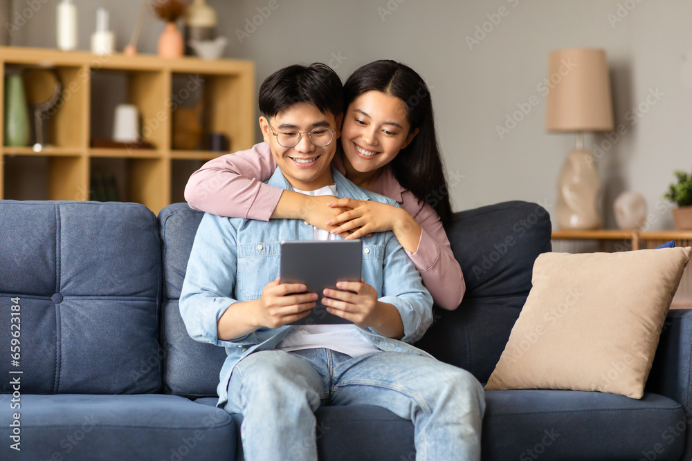 Obraz premium Smiling korean couple websurfing on tablet gadget at home