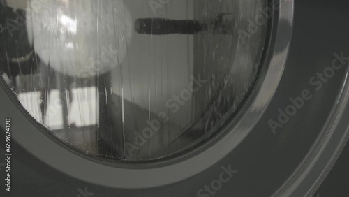 Lavadora de una tintorería con el cristal lleno de gotas de agua