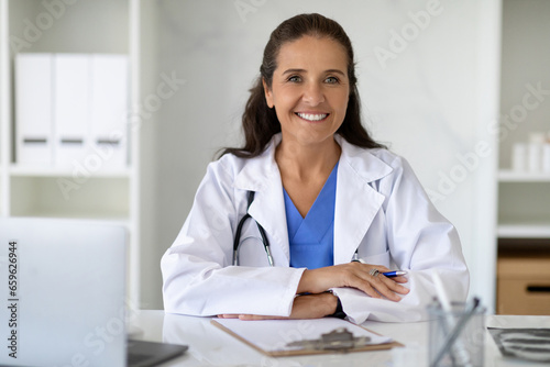 Happy attractive mature lady doctor posing at workplace at clinic