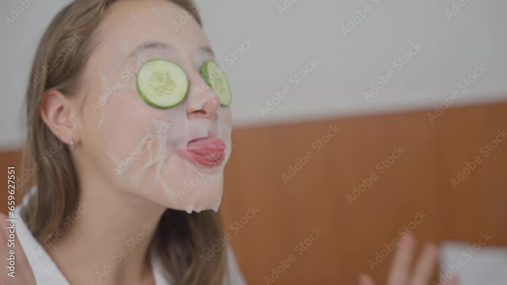 Caucasian woman with facial mask treatment and cucumber on face for skin care and prevent wrinkles making a funny face at home
