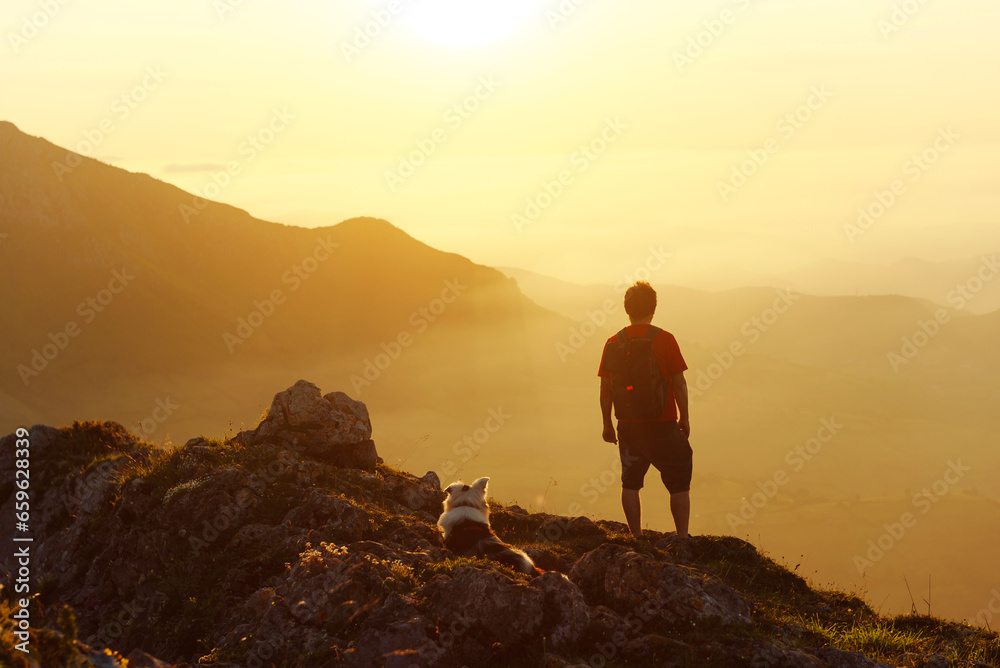 Mountaineer man with backpack contemplates the mountain landscape at sunset after hiking with his dog. Sport, and outdoor adventure. traveling with a pet.