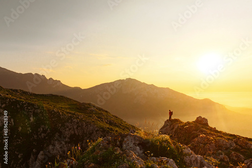 young man walks along the ridge of a mountain with his dog at sunset. Sports, hiking and outdoor adventure