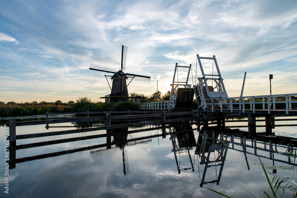 Sunset view over tranquil water in canal with perfect reflection of drawing bridge and one of the iconic 18th-century windmills in Kinderdijk, the Netherlands; UNESCO World Heritage site