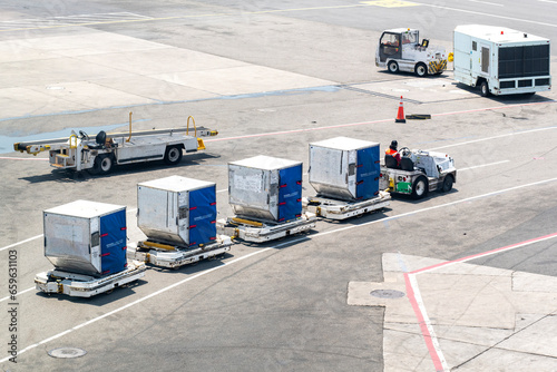 High angle view on tarmac or apron with service road on airport with baggage tractor-trailers (baggage tow tractor), aircraft baggage belt loader or conveyer belt vehicles and mobile generator