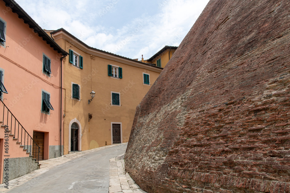 Street view in town of Lari, Italy lined with historic houses with plastered colorful walls and the fortified brick wall of the Castle of Lari (Castello dei Vicari)