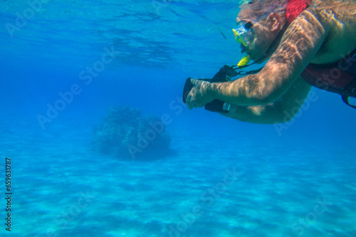 Man with photo camera taking photos and snorkeling underwater by coral reef in the Red sea, Egypt
