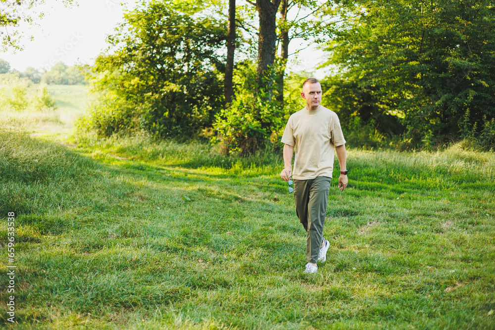 A handsome young man in a beige T-shirt and pants is walking on a green lawn. Relaxation in nature away from the city. A handsome young man in a beige T-shirt and pants is walking on a green lawn. Relaxation in nature away from the city.
