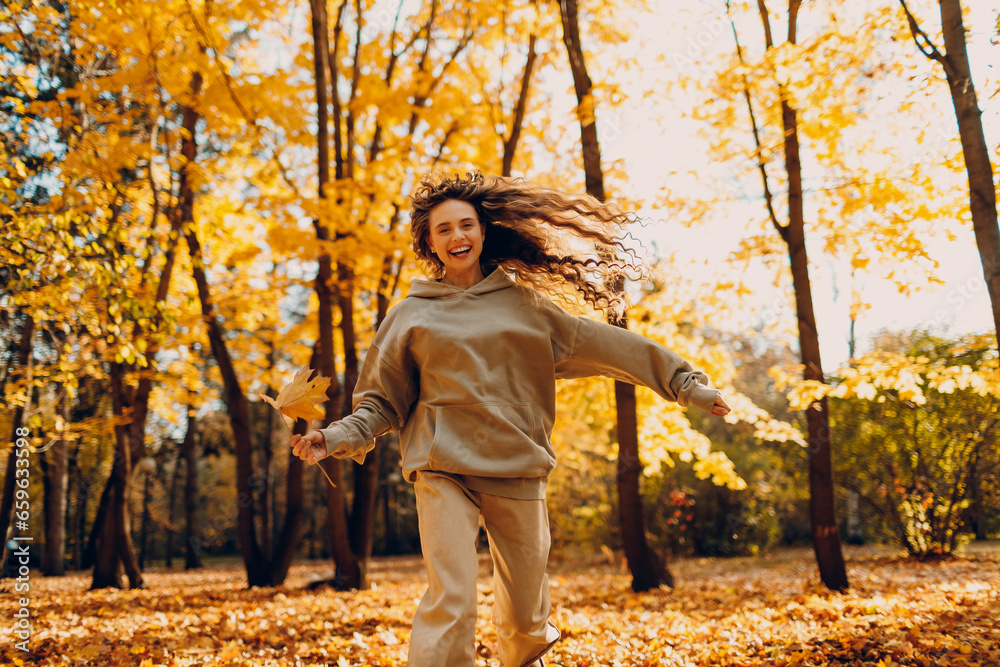 Smiling young woman plays and jumping dancing in the autumn forest with the yellow leaves at sunset Smiling young woman plays and jumping dancing in the autumn forest with the yellow leaves at sunset