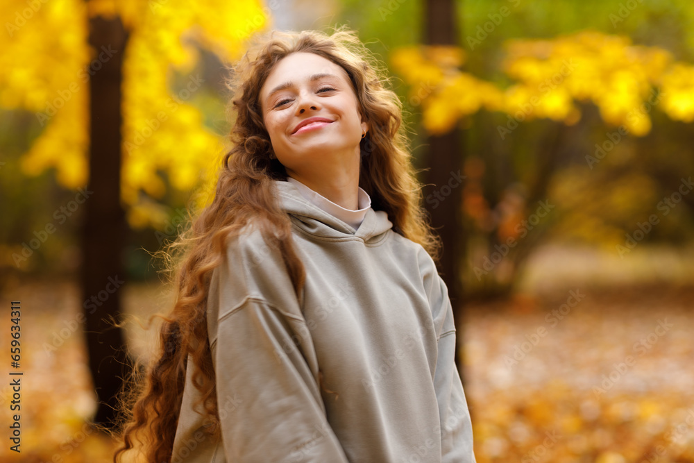 Smiling young woman enjoying the autumn weather in the forest with the yellow leaves at sunset Smiling young woman enjoying the autumn weather in the forest with the yellow leaves at sunset