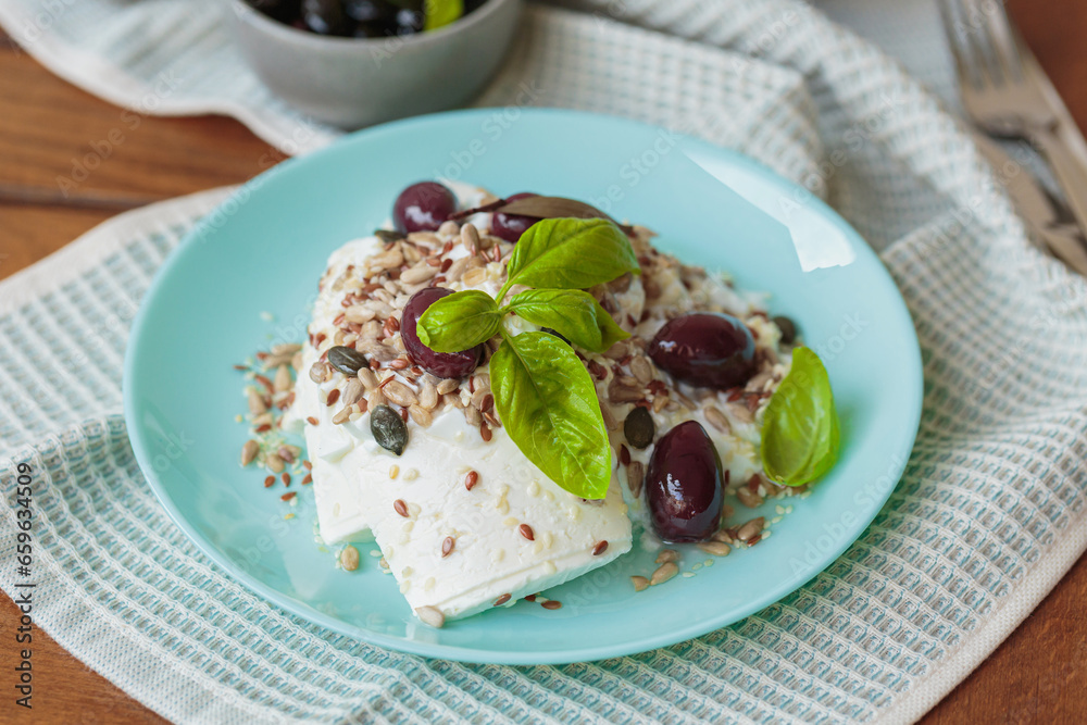 Feta cheese sliced on blue plate with sesame, flax seeds, served with black olives and basil leaves. Delicious and healthy breakfast on terrace Feta cheese sliced on blue plate with sesame, flax seeds, served with black olives and basil leaves. Delicious and healthy breakfast on terrace
