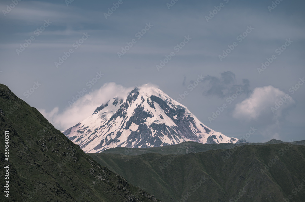An Early morning view of a snowcapped Kazbegi Mountain with clouds surrounding it