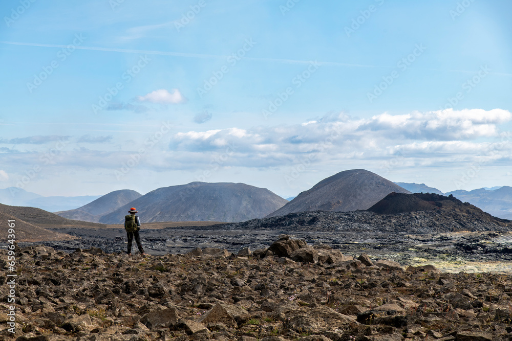 Standing woman overlooking lavafield near mountain Fagradalsfjall with fissure vent of 2021 in Geldingadalir volcano area to the south of Fagradalsfjall mountain, Iceland