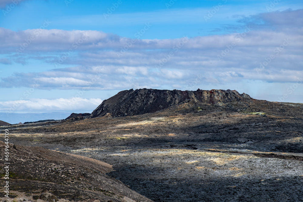 Fissure vent in Geldingadalir volcano area that was active in 2021 near mountain Fagradalsfjall, Iceland with black lava field in forefront against a white clouded blue sky