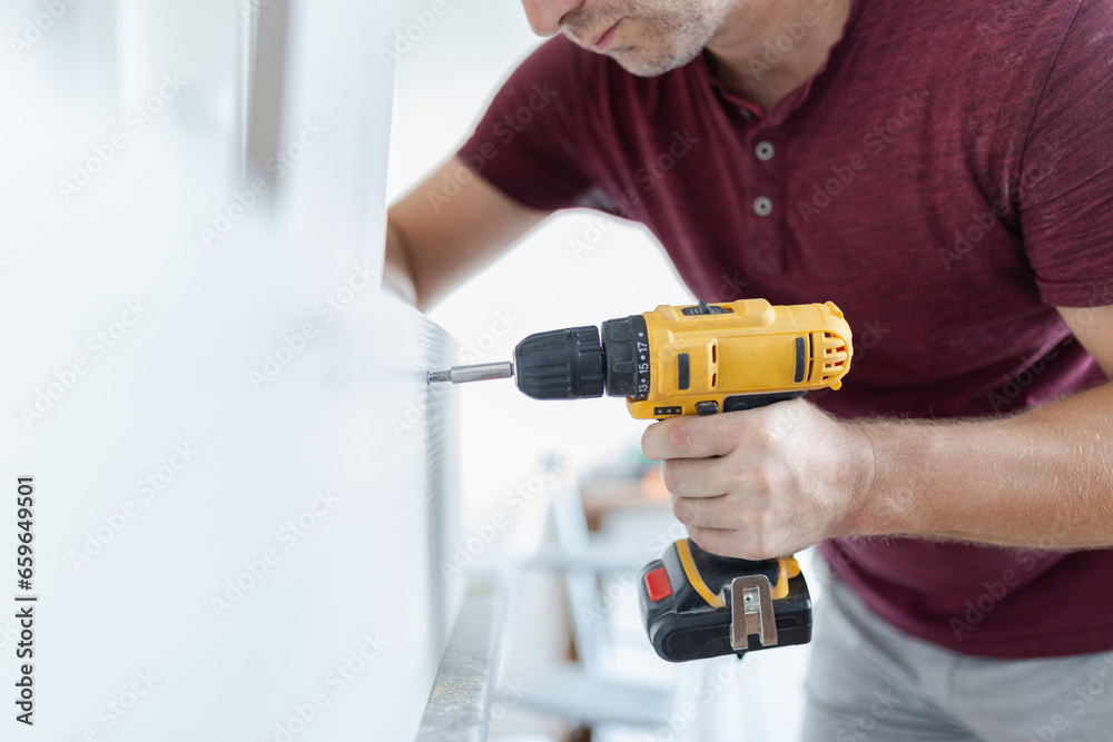 Carpenter installing kitchen chest of drawers by using electrical screwdriver. Home renovation concept.