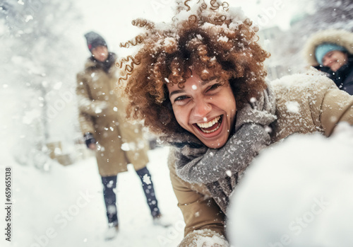 A joyful young individual with curly hair is covered in fresh snow, laughing heartily during a snowy day outdoors.
