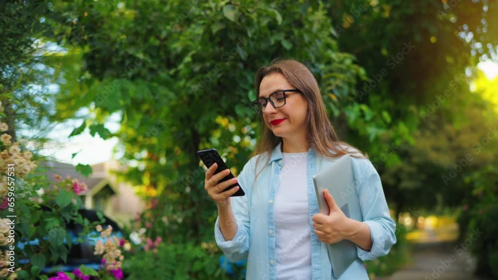 Woman with coffee and smartphone walking through the blooming garden Woman with coffee and smartphone walking through the blooming garden