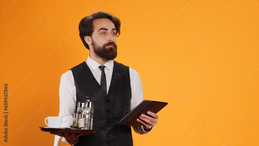 Expert staff member prepares check on tablet while serving in five star restaurant and offer outstanding refined service. Platter with cutlery and modern digital gadget are handled by butler. Expert staff member prepares check on tablet while serving in five star restaurant and offer outstanding refined service. Platter with cutlery and modern digital gadget are handled by butler.