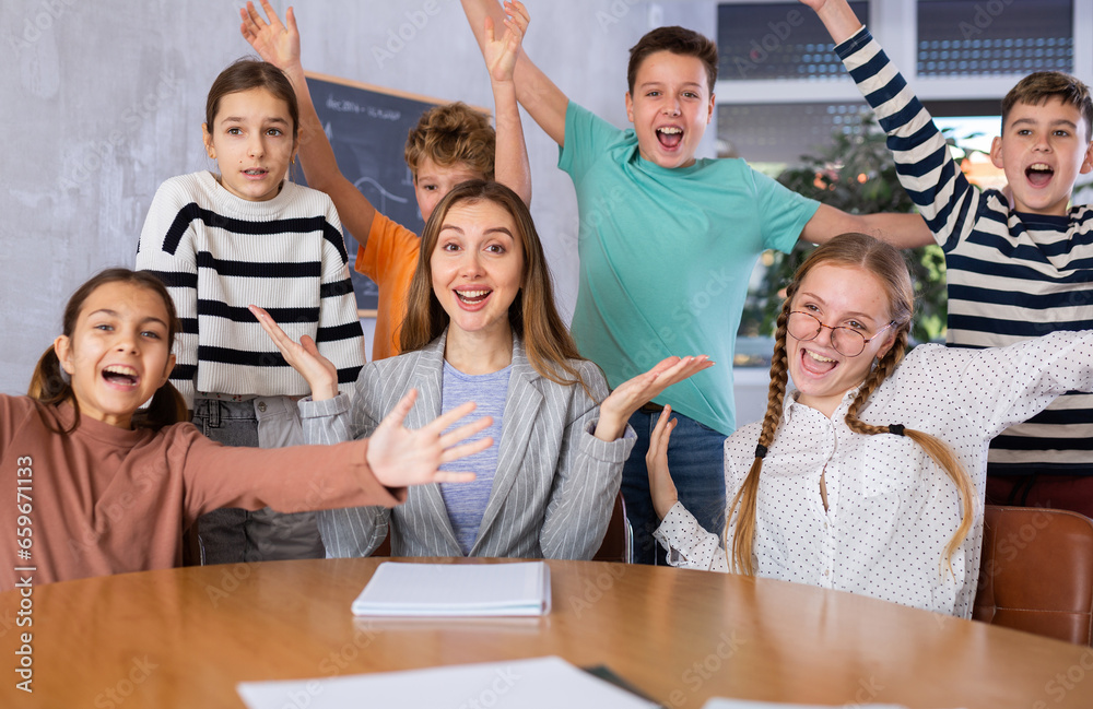 Obraz premium Portrait of friendly positive group of pupils with female teacher sitting in schoolroom
