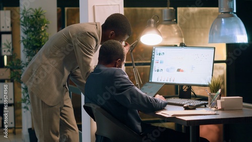 Coworkers in office crosschecking datasets, comparing financial charts and checking business figures during nightshift. Experienced businessmen helping eachother finish project tasks faster photo