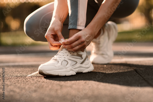An athlete ties a white sneaker in a close-up on a sports field. Fintes in the open air.