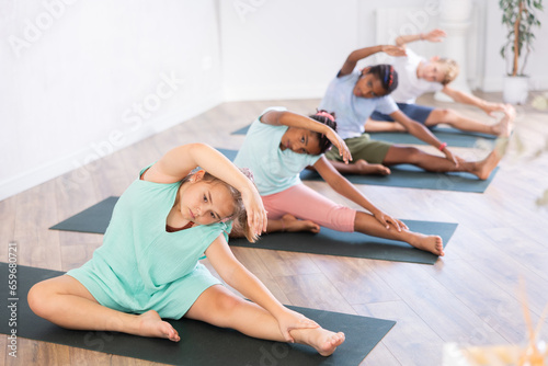 Fototapeta Naklejka Na Ścianę i Meble -  Active children exercising during yoga class in modern fitness center - vakrasana pose