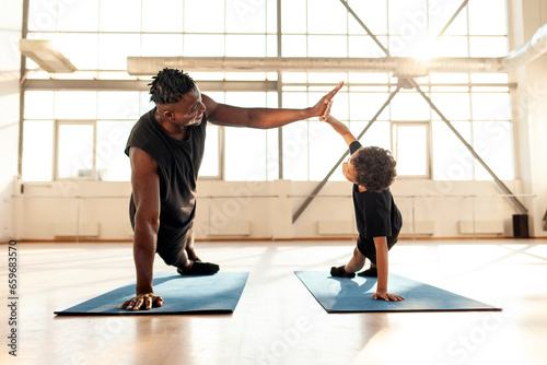 African-American boy doing exercises on yoga mat and doing push-ups with his dad, man training his son