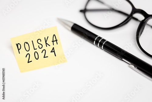 a yellow piece of paper stuck to a white table with the inscription "Polska 2024", next to it are glasses and a pen (selective focus), translation: Poland 2024