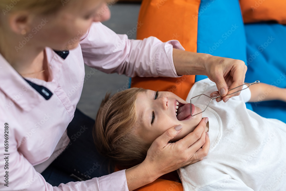 Speech therapy tongue massage to a child little boy with a logopedic probe. Professional female physiotherapist working on speech defects with preschooler boy, exercising correct pronunciation - obrazy, fototapety, plakaty 