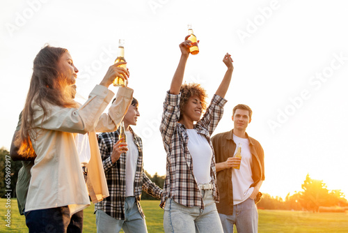 group of multiracial friends at party with bottles of beer dancing and having fun outdoors, group of people singing