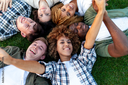group of multiracial young people relax and lie together on grass in the park and smile  team of interracial students