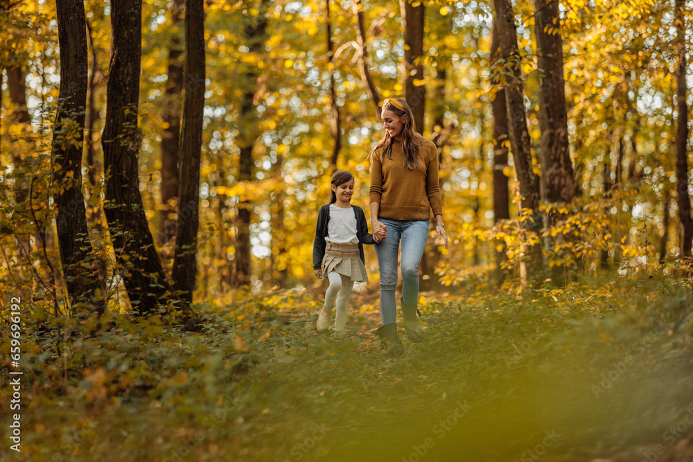 Fototapeta premium Mother and daughter walking in the forest during autumn