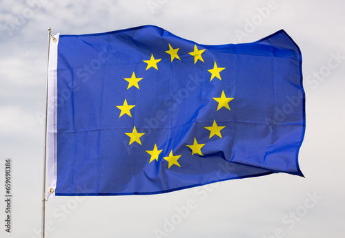 Canvas of flag of European Union flutters on flagpole against gray sky.Close-up, on gray background
