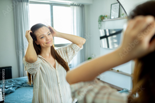 Attractive young woman fixing her hair in front of a mirror in the bedroom