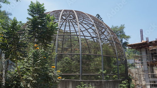 Large metal dome aviary for bird conservation next to a building construction site where crane stand there