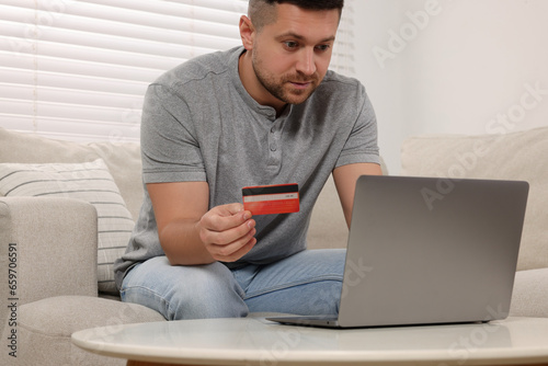 Handsome man with credit card using laptop for online shopping at home