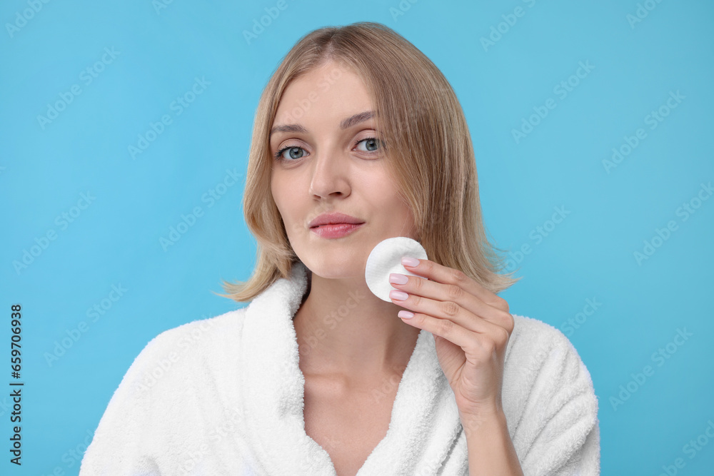 Young woman cleaning face with cotton pad on light blue background Young woman cleaning face with cotton pad on light blue background