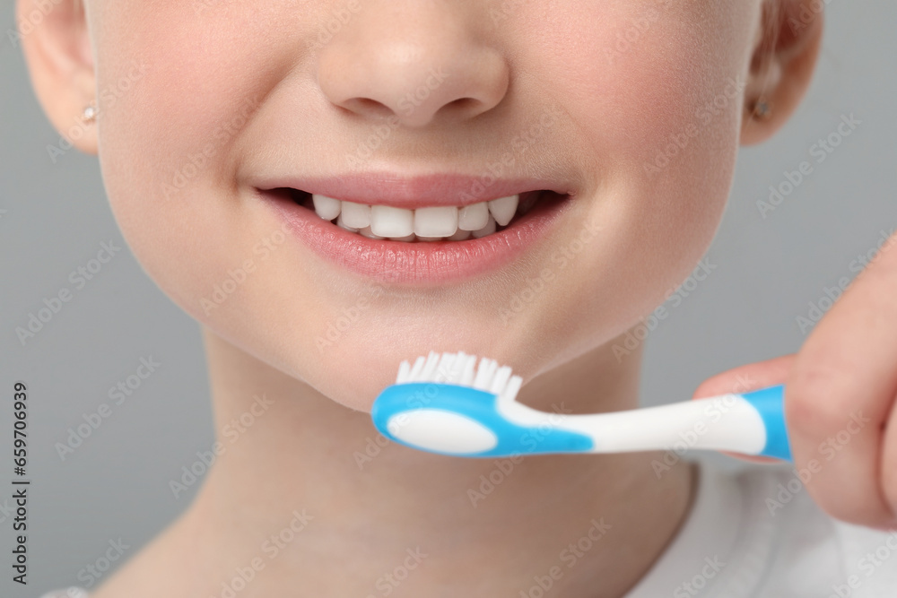 Girl brushing her teeth with toothbrush on light grey background, closeup Girl brushing her teeth with toothbrush on light grey background, closeup