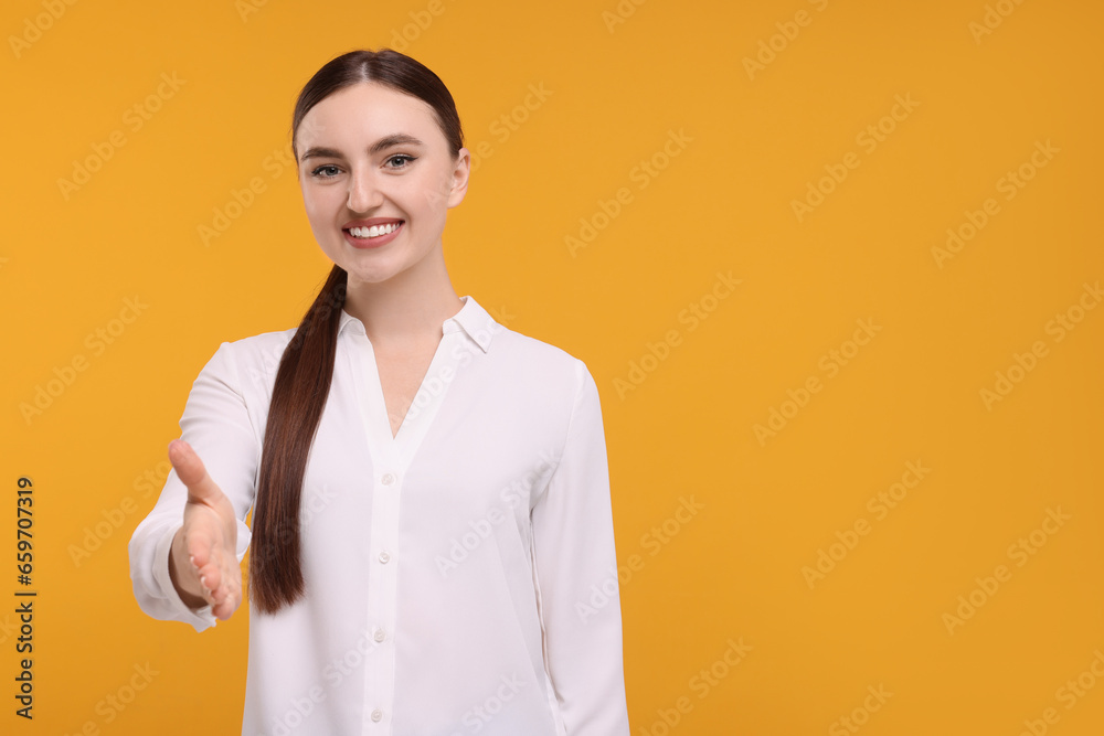 Smiling woman welcoming and offering handshake on orange background. Space for text Smiling woman welcoming and offering handshake on orange background. Space for text