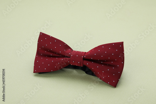 Stylish burgundy bow tie with polka dot pattern on pale green background