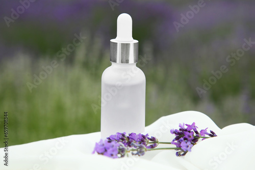 Essential oil and lavender flowers on table covered with white fabric in field