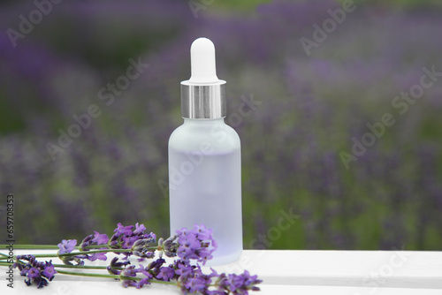 Bottle of essential oil and lavender flowers on white wooden table in field