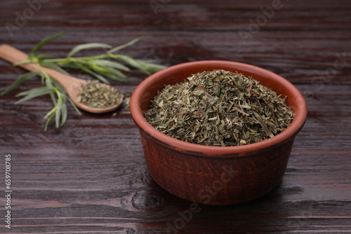 Dry tarragon in bowl on wooden table, space for text