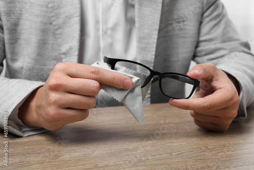 Man wiping glasses with microfiber cloth at wooden table, closeup