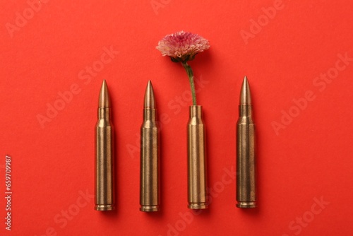 Bullets and cartridge case with beautiful flower on red background, flat lay